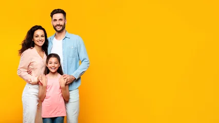 Foto op Plexiglas Happy loving family. European mother and father posing with their daughter on yellow background, panorama, free space © Prostock-studio