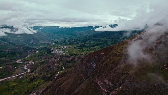 Drone reveals Maca village, passing Pachamarca mountain, with Chivay in the background. Cloudy day after rain