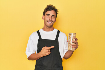 Chef with chickpeas jar on yellow smiling and pointing aside, showing something at blank space.