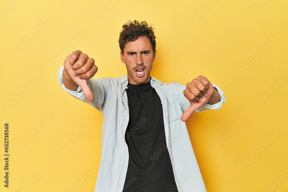 Wall mural Young Latino man posing on yellow background showing thumb down and expressing dislike. - Wall murals