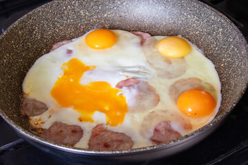 Close-up of a frying pan with hot scrambled eggs and sausage. Freshly prepared breakfast.