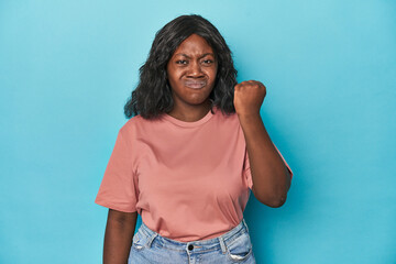 Young african american curvy woman showing fist to camera, aggressive facial expression.