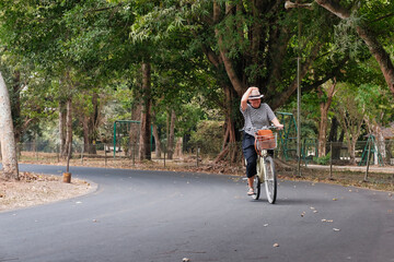 Woman riding bicycle under shady big trees in the park