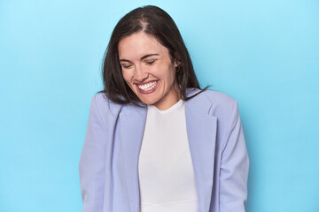 Obraz premium Woman in blue blazer on blue background laughs and closes eyes, feels relaxed and happy.