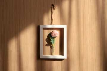 木製の壁に飾られた白い額縁とピンクの造花