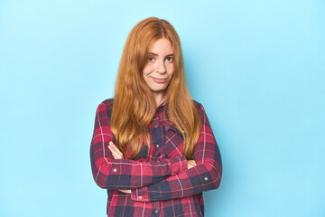 Redhead young woman on blue background suspicious, uncertain, examining you.