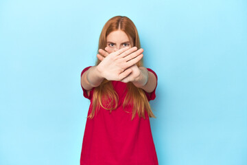 Redhead young woman on blue background doing a denial gesture