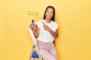 Indonesian woman with roller on ladder on yellow smiling and raising thumb up