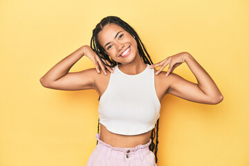 Young Indonesian woman on yellow studio backdrop stretching arms, relaxed position.