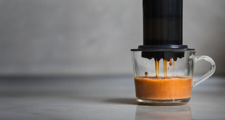 Aeropress coffee close-up, coffee drops pours trought aeropress to cup, gray background - obrazy, fototapety, plakaty