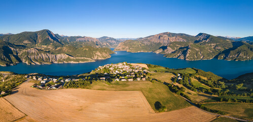 Panoramic aerial view of Serre-Poncon lake with Le Sauze-du-Lac village. Durance Valley in summer. Hautes-Alpes (Alps), France - obrazy, fototapety, plakaty