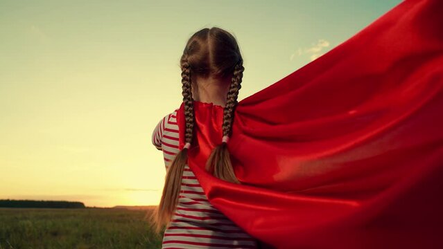 Funny girl with waving red cloak imitates flight in sunset summer field