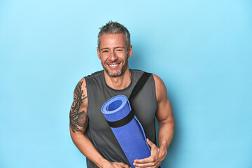 Athlete with a mat on a blue studio backdrop laughing and having fun.