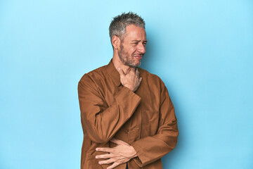 Fototapeta premium Middle-aged caucasian man on blue backdrop suffers pain in throat due a virus or infection.