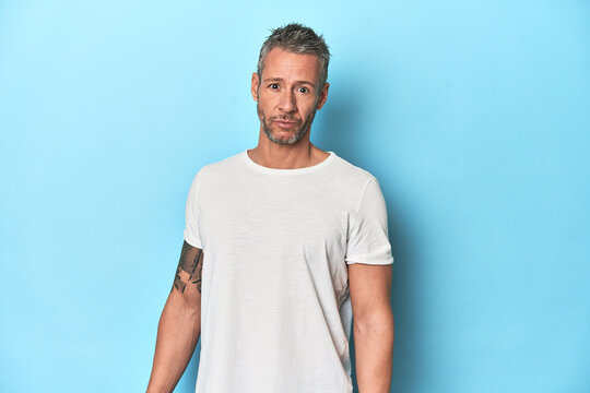 Middle-aged man posing on blue studio backdrop - Powered by Adobe