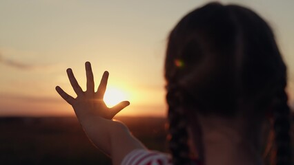 Little girl holding hand against sun silhouette in twilight summer field closeup