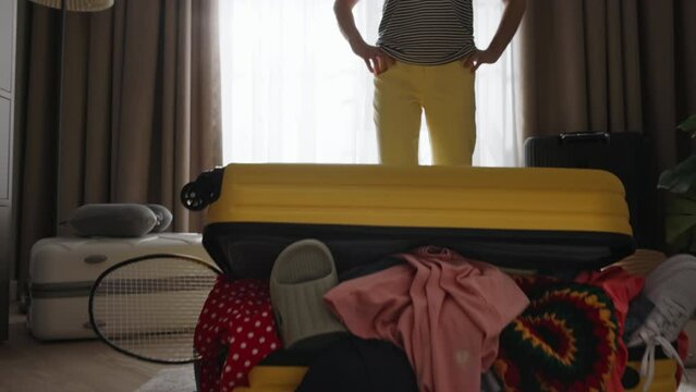 Suitcase with randomly messy packed things, clothes, shoes sticking out of suitcase. Woman not knowing how to put things stuff in order fold pack luggage compactly correctly, to get ready for vacation