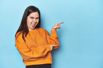 Young Caucasian woman on blue backdrop pointing with forefingers to a copy space, expressing...