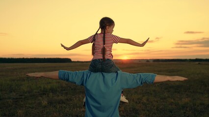 Little daughter sits on father shoulders playing plane in sunset field - Powered by Adobe