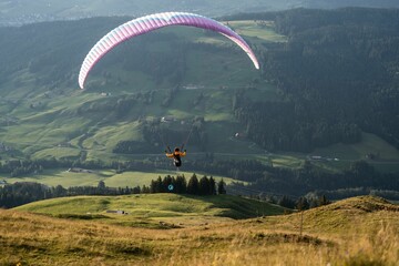 Paraglider in flight, soaring over lush green hills and trees
