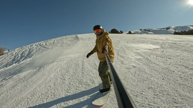 Winter holidays snowboarding with selfie stick in hand between trees in slow motion. Guy makes snow splash while snowboarding and streaming his vlog. Extreme snowboarding in snowy mountains