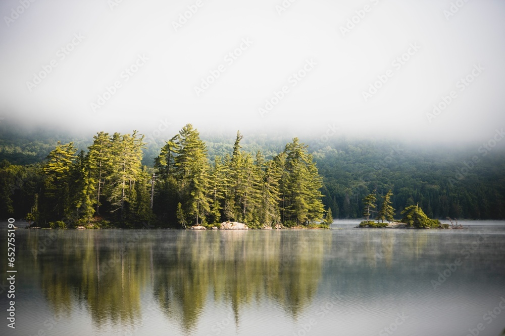 Wall mural Lush green mountains in the distance with a body of water them while a fog hangs overhead