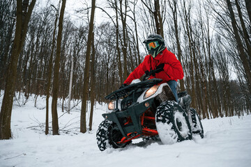 Fototapeta na wymiar Snow, trees, adventure. Man is riding ATV outdoors in the winter forest