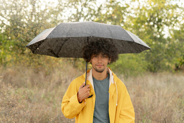 Arabic guy holding umbrella while strolling outside. He is looking at camera with true delight and...