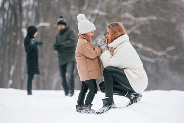 Fototapeta na wymiar Mother and daughter looking at each other. Happy family is outdoors, enjoying snow time at winter together