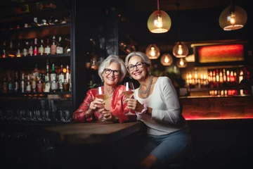 Fotobehang Lady's night out, two middle aged female friends celebrating birthday in bar with white wine © Jasmina