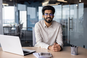 Portrait of a young Indian male designer, engineer sitting in the office at the table and looking...