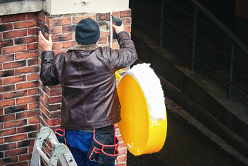 Worker on ladder drilling facade wall, install outdoor LED advertising, mount on wall glowing lightbox and installing wires. Construction worker using cordless drill equipment. .