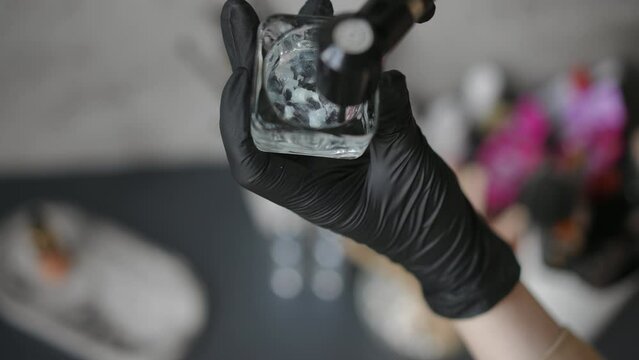High angle view close-up mixing gel with ink mixer in beauty salon. Closeup unrecognizable Caucasian young woman in black gloves preparing for eyebrows coloring procedure indoors
