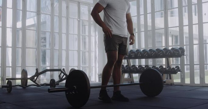 Young multiracial man in sportswear taking a break after weightlifting with barbell at the gym