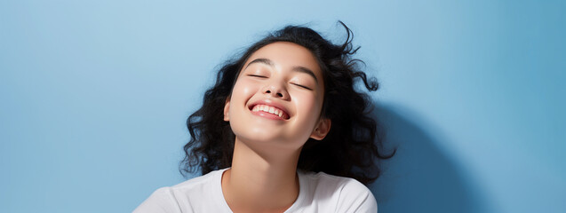 Studio portrait of young laughing Asian girl in white t shirt and blue background
