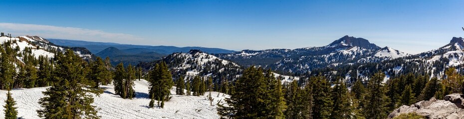 Panoramic shot of hills covered in forests and snow under a blue sky and sunlight