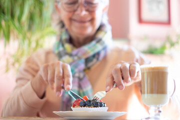 Close up on happy senior woman eating fruit cake in cafe enjoying break or breakfast ignoring diets