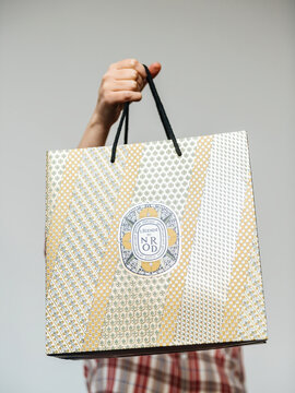 PARIS, FRANCE - DEC 2, 2018: Woman holding golden luxury paper bag from Diptyque a Paris-based luxury goods company that produces a high-end line of scented candles, perfumes, face and body care