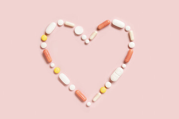 Heart shape made of colorful drug pills and capsules on light pink, top view