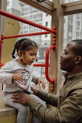 Vertical shot of an Afro-American father playing with his daughter in a playground