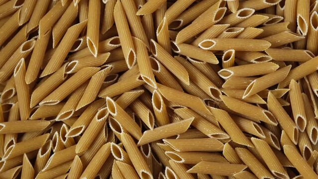Texture of Spelt pasta penne. Uncooked Italian wholegrain Pasta, close-up. 4K Video, Rotating.