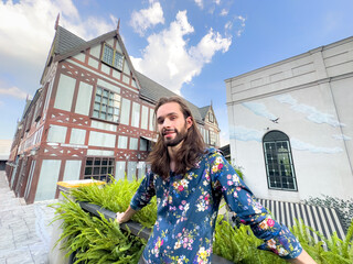 Young hipster man with long hair  standing outside office against building and cock tower