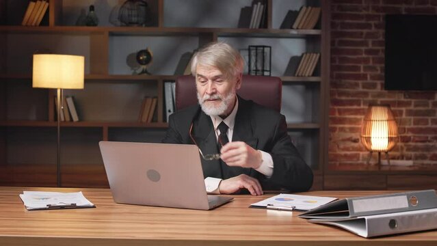 Portrait of senior caucasian male in formal outfit putting reading glasses aside while sitting behind computer in workplace. Stylish general manager checking overall resources of big corporation.