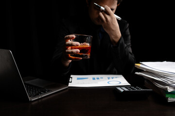 A man drinks whiskey, a businessman relieves stress from work sitting and drinking whiskey in the office after finishing a hard job, a drunk man. Alcohol drinking concept.