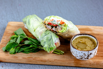 Raw Vietnamese rice spring rolls on wooden board served with soy and chili sauces. 