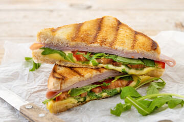 Panini sandwich with ham, cheese, tomato and arugula on wooden table