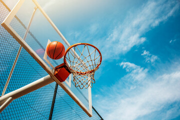 Street basketball ball falling into the hoop against blue cloudy sky. Success, scoring, winning and achieve the goal concept © Yelena
