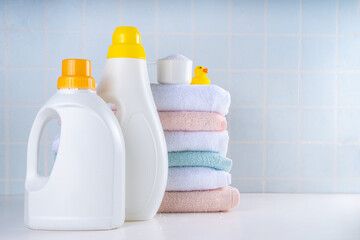 Laundry, washing and cleaning concept. Stack of clean towels, with various detergents - gels, capsules, powder and cute rubber yellow duck, white bathroom background copy space