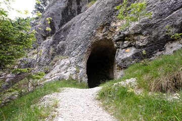 Footpath leading to entrance to the cave in Jura mountains. Black hollow in rock. Mountain tunnel hiking trail, cave enter of dark corridor, Gorges de Court, Switzerland