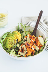 Baked sweet potato wedges salad with cucumber, avocado and creamy tahini dressing, white background.